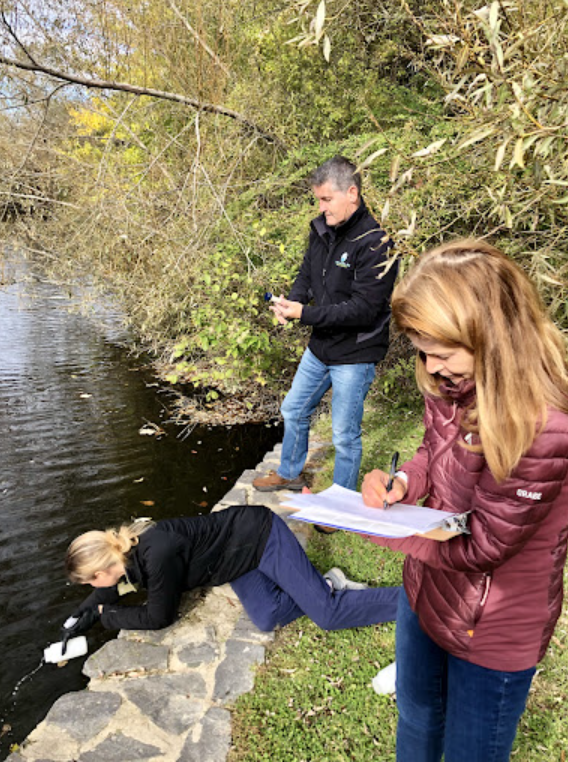 Three people collect data from a body of water. 